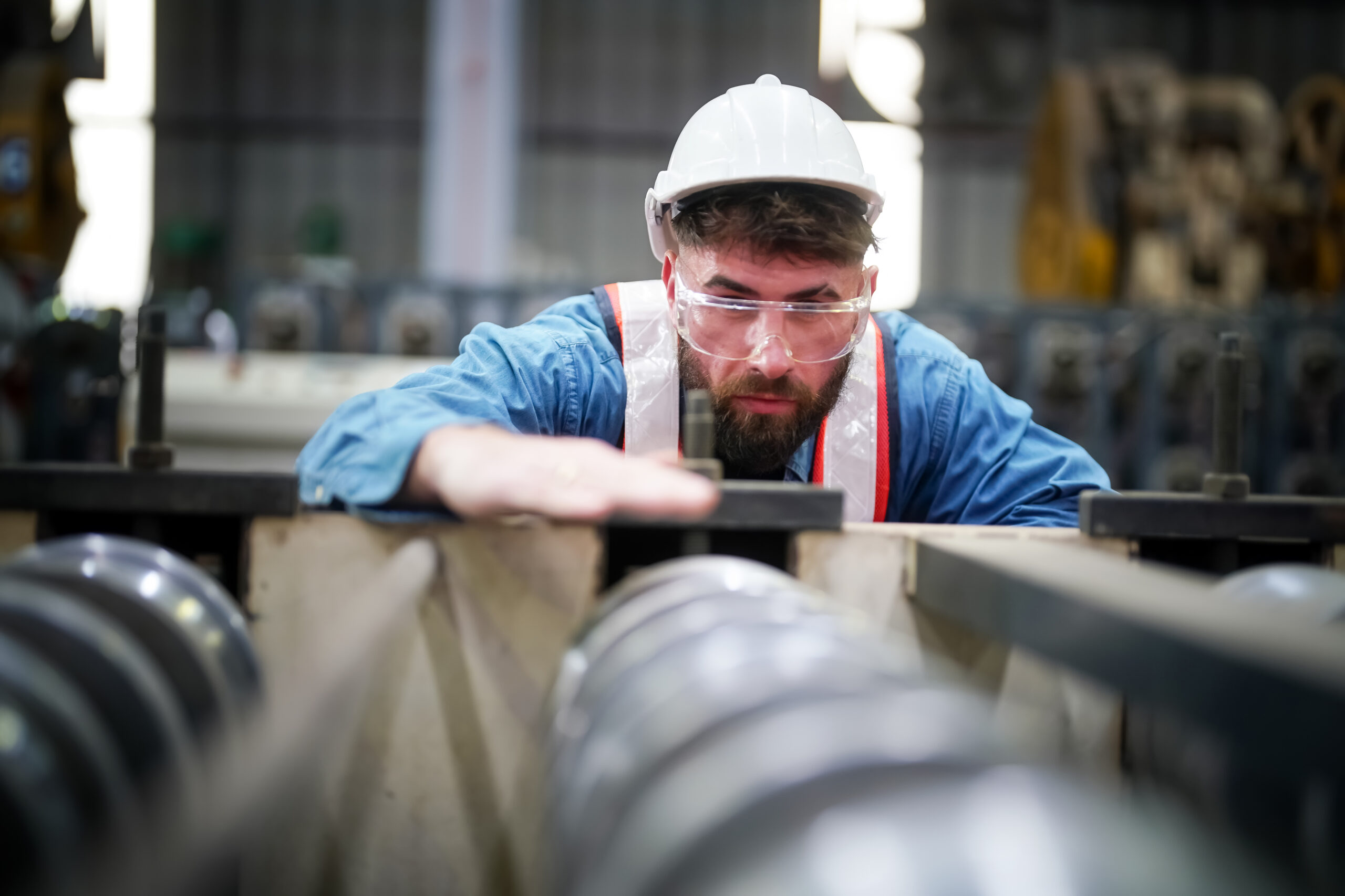 Inside a factory, industrial worker in action on metal press machine holding a piece of steel ready to be worked.